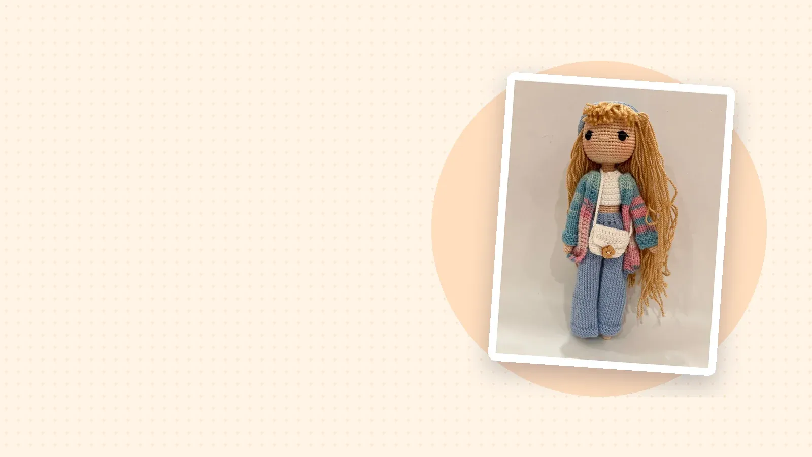 Krem zeminde fotoğraf kartı: mavi pantolonlu, renkli hırkalı uzun sarı saçlı amigurumi bebek