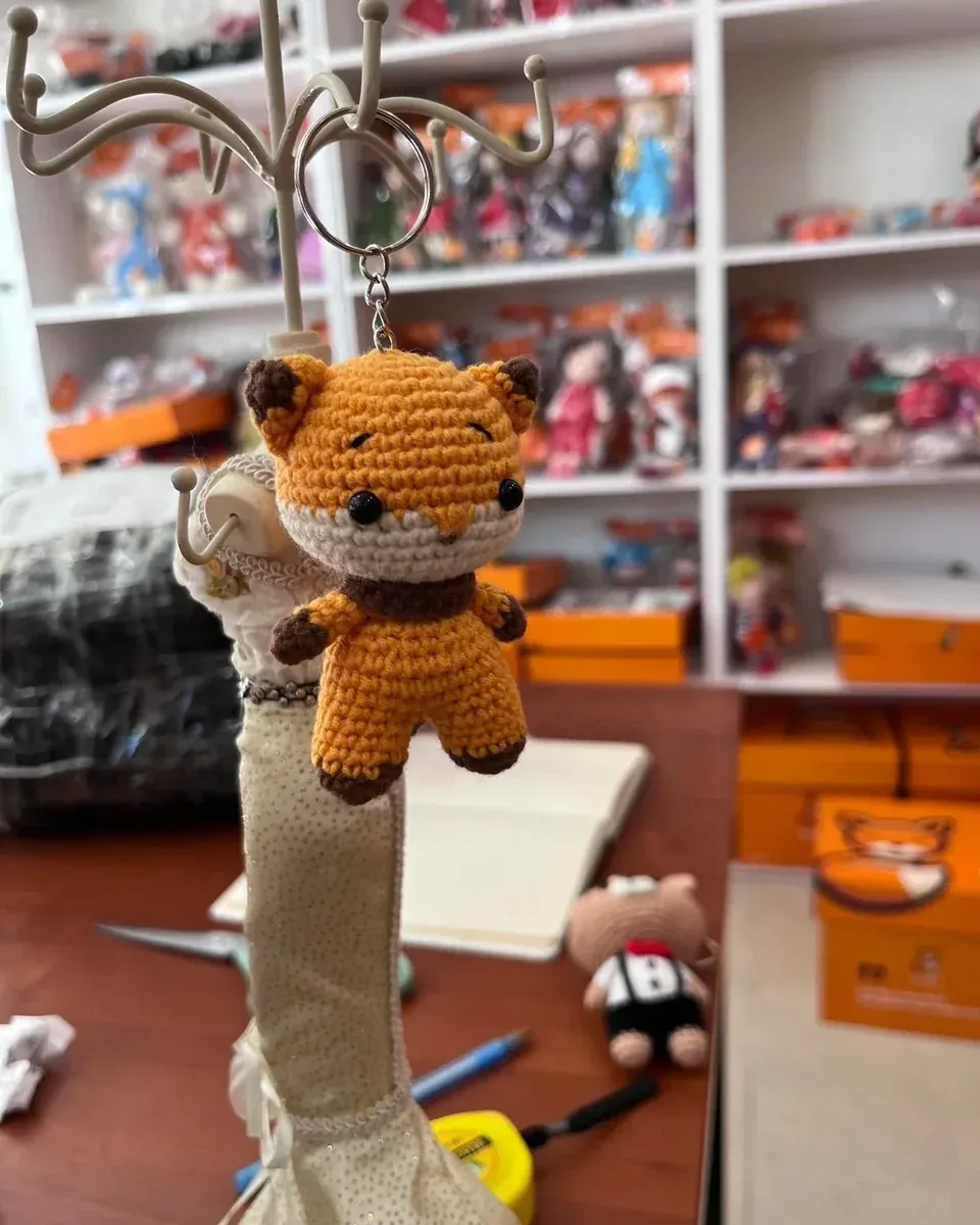 Mağaza rafları önünde askıda turuncu amigurumi tilki anahtarlık