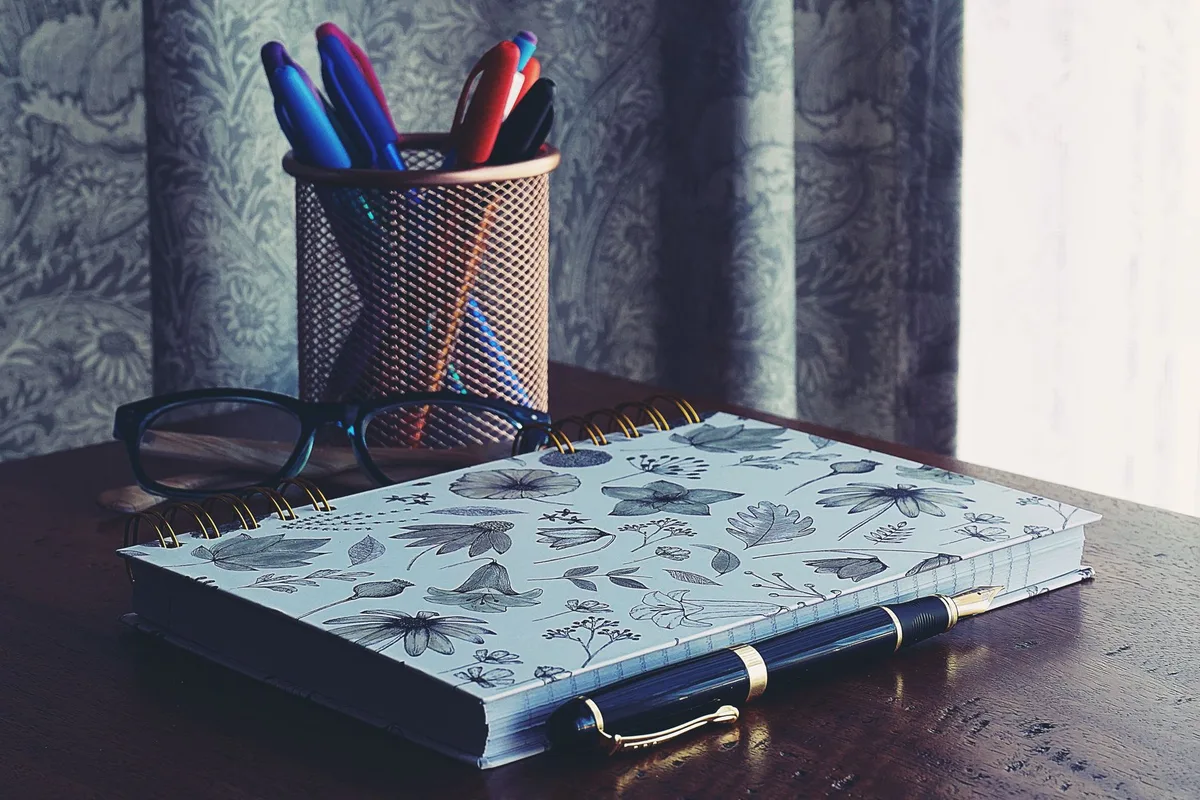 Ahşap masada defter, kalem ve gözlük