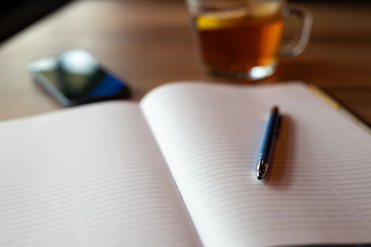 Masada açık defter, kalem ve çay bardağı